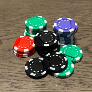 May include: A collection of colorful poker chips in green, purple, red, and black, with white accents. The chips are stacked and arranged on a wooden surface, showcasing a variety of colors and designs. The chips are used for casino games.