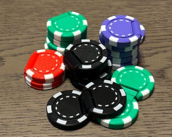 May include: A collection of colorful poker chips in green, purple, red, and black, with white accents. The chips are stacked and arranged on a wooden surface, showcasing a variety of colors and designs. The chips are used for casino games.