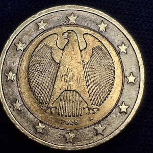 Könnte beinhalten: Eine Zwei-Euro-Münze mit einem detaillierten Adler-Emblem in der Mitte, umgeben von einem Sternenring. Die Münze hat eine goldfarbene Mitte und einen silberfarbenen Außenring. Das Jahr "2008" ist sichtbar.