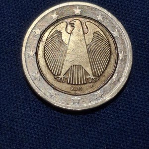 Könnte beinhalten: Eine Zwei-Euro-Münze mit detailliertem Adler-Design, datiert 2011. Die Münze hat einen silbernen Außenring mit Sternen und eine goldfarbene Mitte. Die Münze ist ein Sammlerstück, mit einem Durchmesser von ca. 2,5 cm.