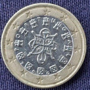 Könnte beinhalten: Eine Ein-Euro-Münze mit silbernem Kern und goldfarbenem Außenring. Die Mitte zeigt ein detailliertes Design mit Text und Symbolen, während der äußere Ring Sterne hat. Die Münze liegt auf einer blauen Oberfläche.