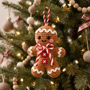 May include: A crocheted gingerbread person ornament in light brown yarn with white wavy icing trim on the head, arms, and legs. It features black bead eyes, pink cheeks, two red buttons on the torso, and a red and white striped hanging loop.