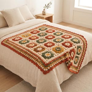 May include: A square crochet blanket featuring a repeating floral granny square pattern in shades of burnt orange, sage green, mustard yellow, and cream. The blanket has a scalloped edge border and is constructed from individual yarn squares.