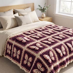 May include: A handmade crochet blanket featuring a repeating square pattern, each containing a three-dimensional butterfly motif in shades of deep plum, light pink, and cream, with a scalloped border edge covering the bed.