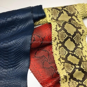 Puede incluir: Primer plano de tres piezas de cuero exótico. Una es azul marino, otra roja brillante y la tercera amarilla con patrones de diamantes marrones. El cuero tiene una apariencia texturizada y escamosa, que sugiere piel de reptil.