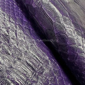 Peut inclure: Gros plan sur un matériau en cuir violet texturé avec un motif en forme d'écailles. Le cuir a un éclat métallique, avec des reflets et des ombres créant de la profondeur. L'effet global est luxueux et accrocheur, adapté à divers projets d'artisanat.