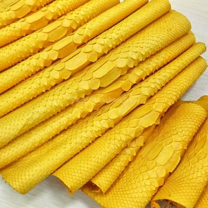 Puede incluir: Primer plano de varias hojas de cuero de piel de serpiente amarillo brillante. El cuero presenta un patrón texturizado y escamoso, dispuesto en capas diagonales. El color es un amarillo vibrante y soleado, con un efecto llamativo.