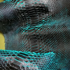 Op de afbeelding: Close-up van zwart leer met een slangenleerpatroon, geaccentueerd met turquoise accenten. De textuur is gedetailleerd en toont de schubben en ribbels van het materiaal. Het algehele effect is luxueus en exotisch.