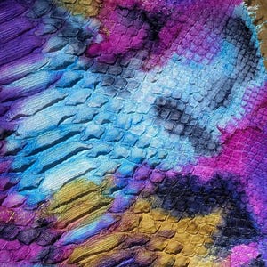 Puede incluir: Primer plano de un trozo de tela con un patrón de escamas en colores vibrantes. Los colores incluyen tonos de azul, morado, dorado y rosa, creando un efecto tie-dye. La textura parece áspera y texturizada.