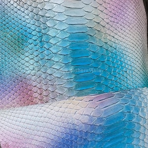 Puede incluir: Primer plano de un trozo de piel de serpiente iridiscente. Las escamas hacen la transición del azul al morado y al blanco, creando un efecto degradado. La textura de las escamas es claramente visible, con un brillo sutil.