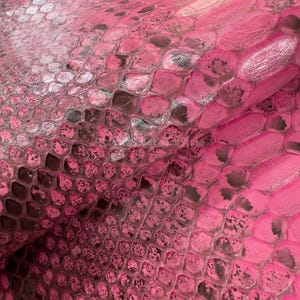May include: A close-up view of a pink snakeskin pattern. The texture shows a scale-like design with darker, mottled accents, creating a detailed surface. The colour is a bright, saturated pink.