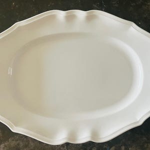 Op de afbeelding: Een witte, ovale serveerschaal met een geschulpte rand. De schaal heeft een glad, glanzend oppervlak en een licht verhoogde rand. Dit elegante gerecht is perfect voor het serveren van hapjes, hoofdgerechten of desserts.