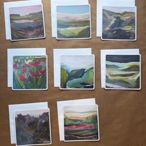 May include: A collection of eight square greeting cards featuring abstract landscape and floral paintings. Each card displays unique brushwork in varied color palettes including greens, pinks, reds, and blues, with white envelopes placed behind each card.