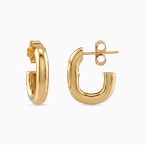 Peut inclure: Une paire de boucles d'oreilles créoles dorées en forme de U. Les boucles d'oreilles ont une surface polie et réfléchissante et une fermeture à tige et à fermoir. Le design est de style simple et moderne.
