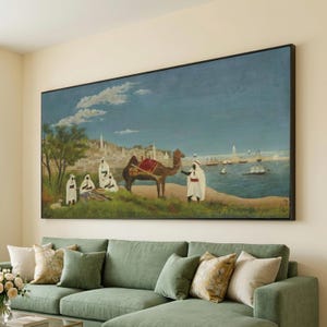 Puede incluir: Gran pintura de paisaje enmarcada que representa una escena de Oriente Medio con figuras con túnicas blancas, un camello y barcos en el agua. La obra presenta un cielo azul y una ciudad costera al fondo. La pintura se exhibe sobre un sofá seccional verde.