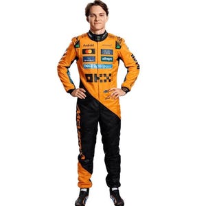 以下が含まれることがあります： オレンジと黒を基調としたマクラーレンのレーシングスーツを着た人物。スポンサーのロゴも入っている。全身を覆うスーツで、両手を腰に当てて立っており、黒いレーシングブーツを履いている。マクラーレンのロゴが見える。