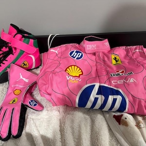 May include: Pink racing suit, gloves, and shoes with various sponsor logos, including HP, Shell, and Ferrari. The gloves have black accents and the shoes have green and black details. The suit has the IBM logo on the collar.