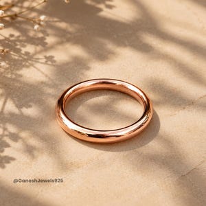May include: A polished rose gold band ring with a smooth, rounded surface and a high-shine metallic finish. The ring is circular and features a simple, solid design. The text GaneshJewels925 is visible in the lower left corner of the image.