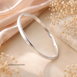 May include: A polished silver bangle bracelet with a smooth, rounded surface and a reflective metallic finish. The jewelry piece is circular in shape and features a clean, simple design. The text @GaneshJewels925 is visible in the lower left corner.