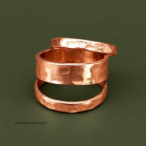 Puede incluir: Tres anillos de cobre apilados que presentan una textura martillada distintiva en sus superficies. Los anillos varían en ancho, con una banda más ancha colocada entre dos bandas más delgadas, todas con un acabado metálico rojizo.