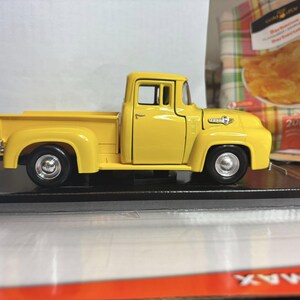 Peut inclure: Modèle réduit jaune vif d'un pick-up Ford vintage. Le camion a des roues noires avec des jantes argentées et un intérieur détaillé. Le modèle est présenté sur une base noire, mettant en valeur son design classique.
