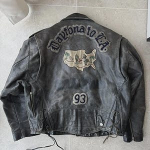 May include: Distressed black leather jacket with the text "Daytona to L.A." and a map graphic on the back. Features a "93" patch and side lacing details. A vintage-style motorcycle jacket.
