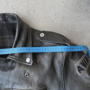 May include: Black leather jacket with a zipper closure and a small patch that reads "AVIA". The jacket is measured with a blue measuring tape. The jacket's shoulder width is approximately 18 inches.