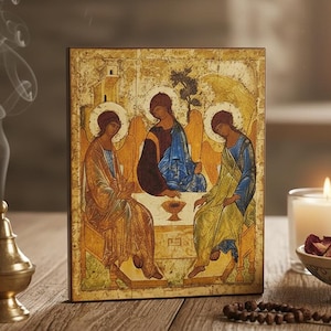 Pode incluir: Ícone religioso retratando três figuras em vestes, sentadas em volta de uma mesa. O ícone está sobre uma superfície de madeira, com uma vela acesa, um queimador de incenso e uma tigela decorativa. As figuras têm auréolas.