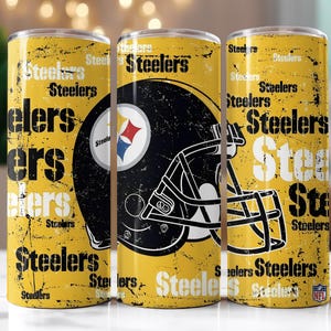 Op de afbeelding: Drie gele bekers met een distressed design met het woord "Steelers" in zwart en wit. Een zwarte voetbalhelm met het Steelers-logo is gecentreerd op een beker. Het NFL-logo is zichtbaar.