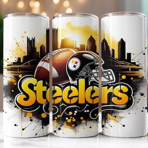 Op de afbeelding: Witte tumbler met een voetbal, helm en het woord "Steelers" in geel en zwart. Het ontwerp bevat een silhouet van een stadsgezicht en abstracte verfspatten, wat een dynamische sportthema-esthetiek cre&euml;ert.