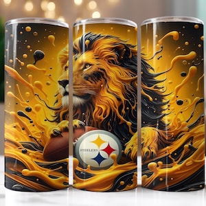 Op de afbeelding: Drie roestvrijstalen bekers met een leeuwenontwerp, een voetbal en het Pittsburgh Steelers-logo. De leeuw is goud en zwart, met een spatteffect. De bekers zijn cilindrisch.