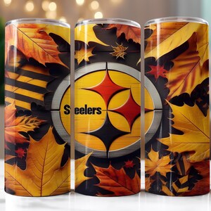 Op de afbeelding: Drie roestvrijstalen bekers met het logo van de Pittsburgh Steelers, omringd door gele, oranje en rode herfstbladeren. Het woord "Steelers" is zichtbaar op de bekers.