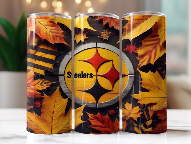 Op de afbeelding: Drie roestvrijstalen bekers met het logo van de Pittsburgh Steelers, omringd door gele, oranje en rode herfstbladeren. Het woord "Steelers" is zichtbaar op de bekers.