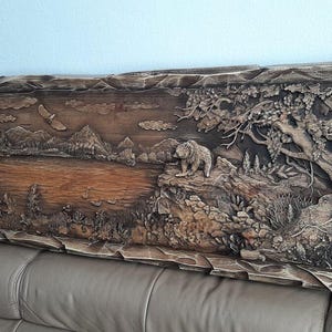 May include: A detailed, carved wooden wall art piece depicting a forest scene with a bear, lake, mountains, and trees. The artwork is framed with a textured border and has a natural, rustic appearance.