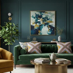 May include: A stylish living room featuring a green velvet sofa, a gold coffee table, and abstract artwork. Two cushions with a geometric design adorn the sofa. The walls are a deep teal, and a potted plant adds a natural element.