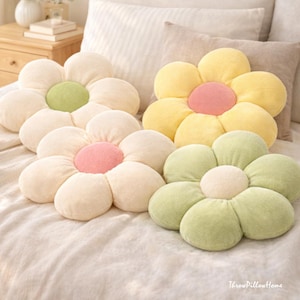 Könnte beinhalten: Vier blütenförmige Kissen in Creme, Gelb und Grün mit rosa und grünen Zentren. Die Kissen sind auf einem Bett mit einer neutralfarbenen Bettdecke und Kissen angeordnet. Der Text "ThrowPillowHome" ist unten rechts sichtbar.