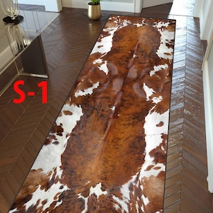 May include: A rectangular rug with a brown and white cowhide pattern. The rug is placed on a dark wood floor in a hallway. The text "S-1" is visible in the image.