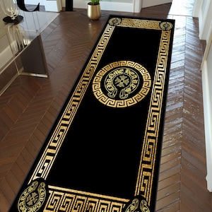 Könnte beinhalten: Schwarzer rechteckiger Teppich mit goldener geometrischer Bordüre und goldenem Mittelwappen. Der Teppich hat ein sich wiederholendes griechisches Schlüsselmuster und ein dekoratives Emblem mit dem Text "Chrome Hearts".