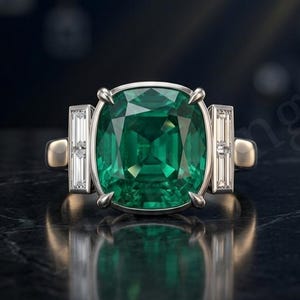 Peut inclure: Une bague argentée ornée d'une grande pierre précieuse verte taille coussin au centre, fixée par quatre griffes. La bague est flanquée de chaque côté d'une pierre claire rectangulaire taille baguette sertie sur un anneau en métal poli.