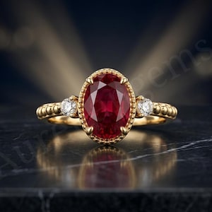 Könnte beinhalten: Ein Goldring mit einem großen, oval geschliffenen, tiefroten Rubin in der Mitte, der von einem perlenartigen Metallrand umgeben ist. Der Ring wird durch zwei kleine, rund geschliffene, klare weiße Diamanten an den Seiten ergänzt.