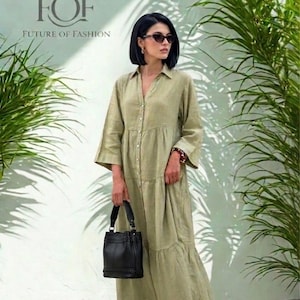 May include: A woman wearing a sage green button-down maxi dress, sunglasses, and brown sandals, holding a black handbag. The dress has a tiered skirt and three-quarter sleeves. The image includes the text "FOF FUTURE OF FASHION".