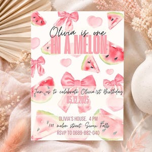 Puede incluir: Una invitación de color claro con un diseño de acuarela con rodajas de sandía, lazos rosas y corazones. El texto dice "Olivia is one IN A MELON" e invita a los invitados al primer cumpleaños de Olivia el 05.12.2025. Incluye dirección e información RSVP.