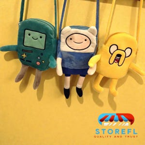 May include: Three plush character crossbody bags in teal, blue, and yellow. The teal bag resembles a video game console, the blue bag has a character with a white hat, and the yellow bag is a cartoon dog. All have long straps.