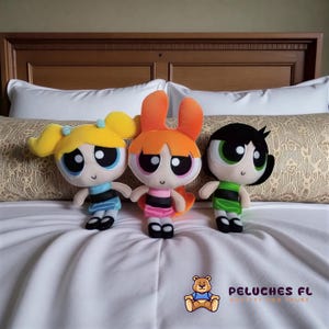 Puede incluir: Tres muñecos de peluche de los personajes de Las Supernenas: Burbuja, Pétalo y Cactus. Burbuja tiene coletas rubias y un vestido azul. Pétalo tiene pelo naranja y un vestido rosa. Cactus tiene pelo negro y un vestido verde.