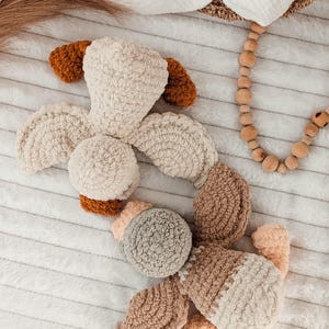 Puede incluir: Un juguete de perro de peluche hecho a mano en crema, marr&oacute;n y beige. El juguete presenta una cabeza redondeada, orejas ca&iacute;das y un cuerpo segmentado. El material suave y texturizado es visible en un primer plano, lo que sugiere una sensaci&oacute;n acogedora y t&aacute;ctil. El juguete es para beb&eacute;s y ni&ntilde;os.