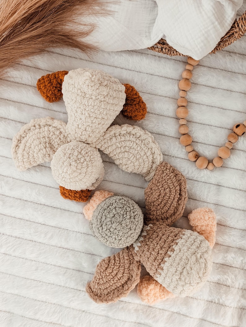 Puede incluir: Un juguete de perro de peluche hecho a mano en crema, marr&oacute;n y beige. El juguete presenta una cabeza redondeada, orejas ca&iacute;das y un cuerpo segmentado. El material suave y texturizado es visible en un primer plano, lo que sugiere una sensaci&oacute;n acogedora y t&aacute;ctil. El juguete es para beb&eacute;s y ni&ntilde;os.