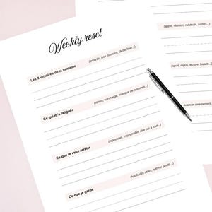 Peut inclure: Un planificateur hebdomadaire avec les titres "Weekly reset" et "Plan your week" en écriture élégante. Les pages comportent des lignes pour les notes et des invites comme "Mes 3 priorités" et "Ce qui m'a fatiguée". Un stylo noir repose sur la page.