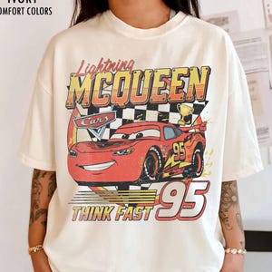 Peut inclure: T-shirt ivoire avec un motif de Flash McQueen du film Cars. Le design comprend le texte "Lightning McQueen", "Cars", "95" et "Think Fast". Le t-shirt est de style confort.