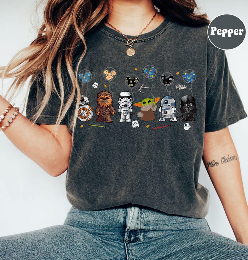 Peut inclure: T-shirt gris fonc&eacute; avec des personnages de dessins anim&eacute;s Star Wars tenant des ballons. Les personnages incluent BB-8, Chewbacca, un Stormtrooper, Grogu, R2-D2 et Dark Vador. Les ballons ont divers motifs, dont des oreilles de Mickey Mouse et des plan&egrave;tes.