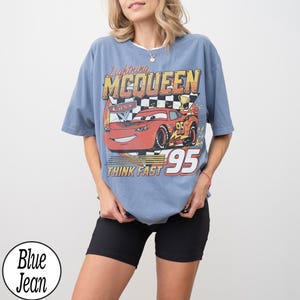 Peut inclure: T-shirt bleu avec un motif de Flash McQueen du film Cars. Le graphisme comprend le texte "Lightning McQueen", "Cars", "95" et "Think Fast". Le t-shirt a des manches courtes et un col rond.